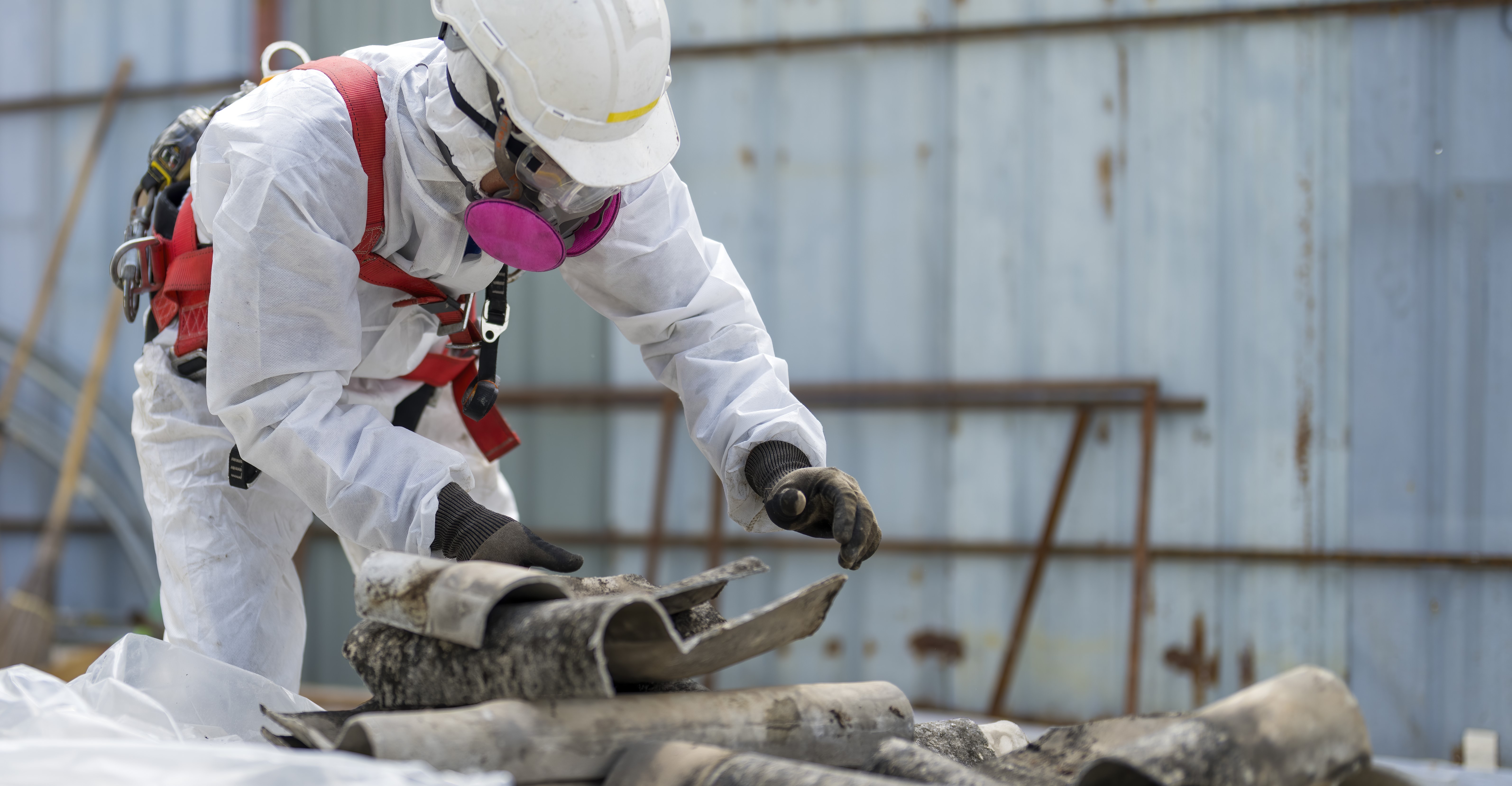 Työntekijä turvapuvussa siivoaa asbestia katosta