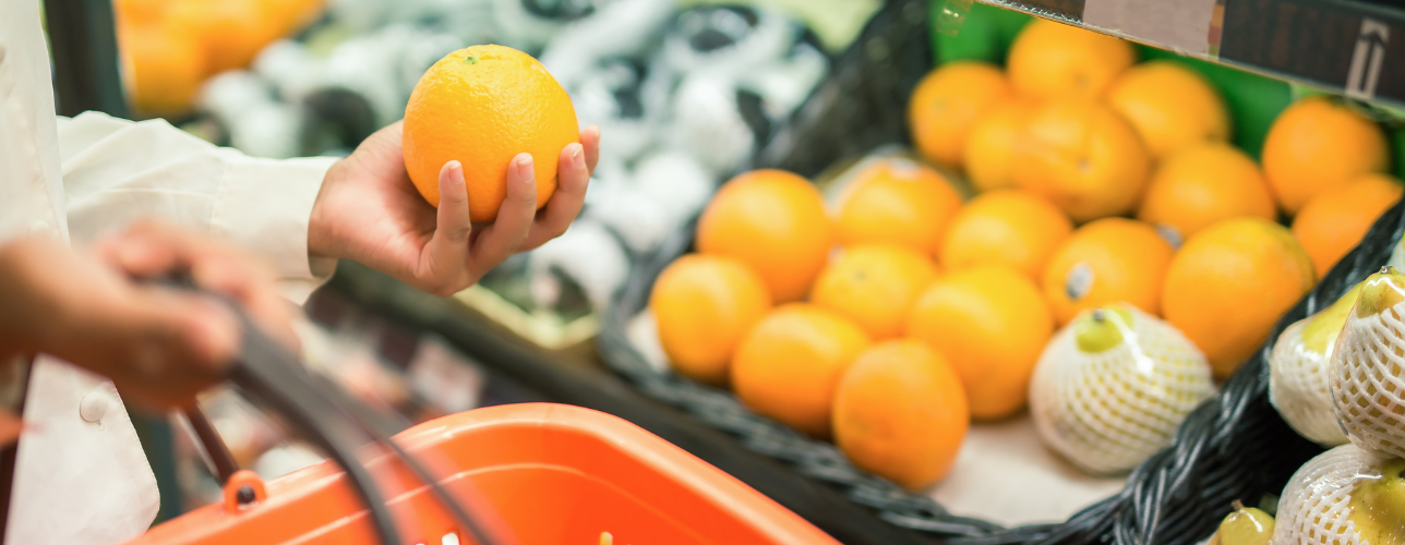 Naisen käsi pitelee appelsiinia ruokakaupassa