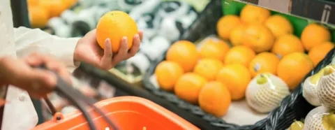 Naisen käsi pitelee appelsiinia ruokakaupassa