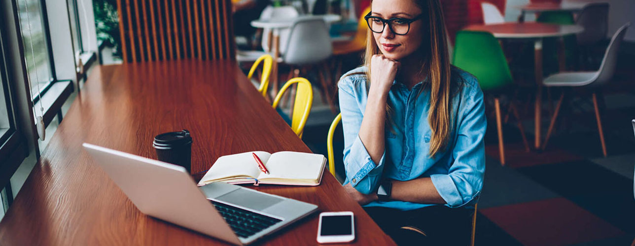 Silmälasipäinen nainen katsoo tietokoneen ruutua ja istuu työtuolissa