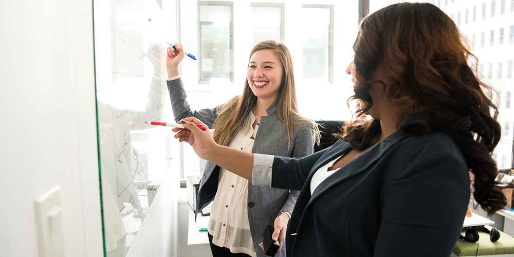 Kaksi kollegaa kirjoittaa valkotaululle